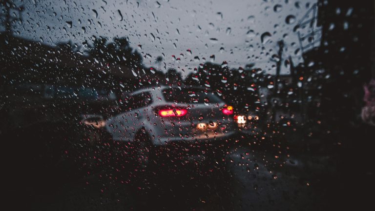Moody street scene through a rain-covered window in Palakkad, India, capturing evening traffic.